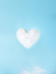 Levitating white heart shaped cloud and white snowflakes falling from it in blue sky