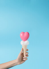 Pink heart shaped icecream with cloudy creme held in hand in blue background
