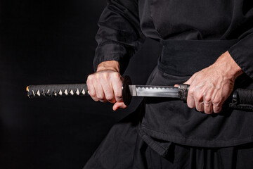 The samurai holding a Japanese katana sword. Photo of a warrior dressed in black clothes in low key...