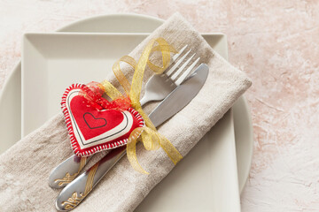Festively served table for Valentine's Day with a plate, fork and knife, red hearts and ribbon on a light  background