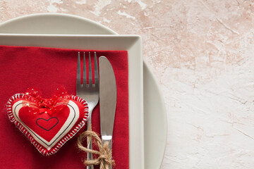 Festively served table for Valentine's Day with a plate, fork and knife, red hearts and ribbon on a light  background