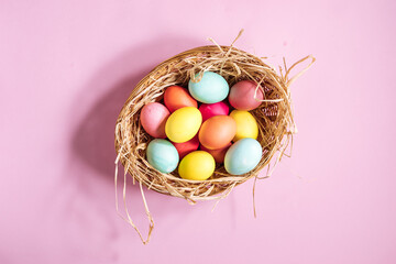 Easter eggs in nest with yellow straw. Very colorful and happy concept. Placed on a pink background. Happy easter 