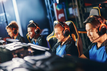 Team of four professional cybersport gamers wearing headphones participating in eSport tournament,...