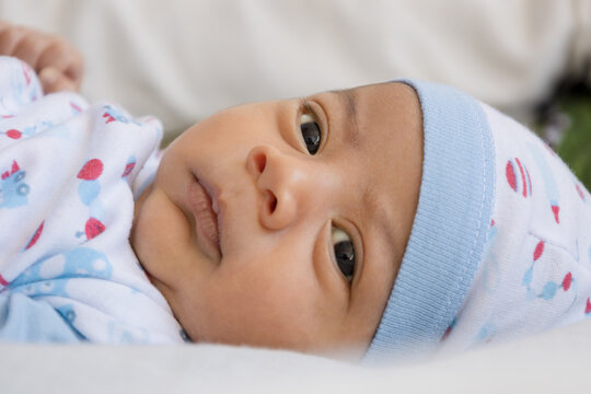 face of tender and beautiful latin baby with open eyes and happy expression, lying on his bed wearing a hat, newborn lifestyle, new life and infant care