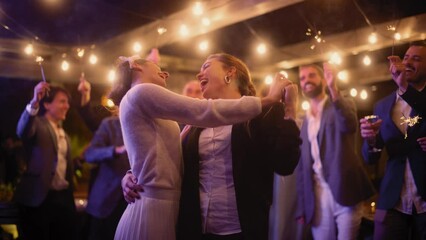 Beautiful Happy Lesbian Couple Celebrate Wedding at an Evening Reception Party with Diverse Multiethnic Friends. Queer Newlyweds Dancing and Kissing at a Restaurant Venue. LGBTQ Relationship Goals.