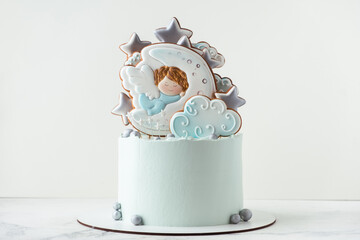 Christening cake with blue cream cheese frosting decorated with gingerbread cookies on the white background. Little baby angel sleeping on the moon. Baby born celebration.