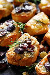 Crostini of sliced baguette with the addition of grapes, seasoned with herbs and honey on a dark background, close-up view.