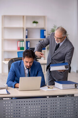 Obraz premium Old male boss and young male employee working in the office