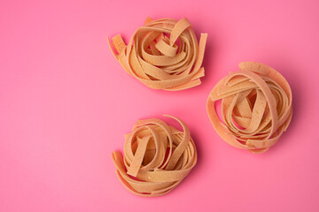 Three nests of Raw tagliatelle on a pink background, pasta nests, egg paste nests