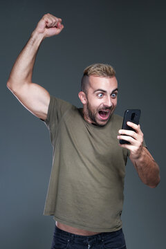 Excited young man receiving winning news on his phone, celebrating and feeling victorious, jumping for joy, studio image