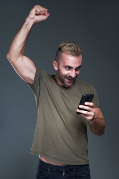 Excited young man receiving winning news on his phone, celebrating and feeling victorious, jumping for joy, studio image