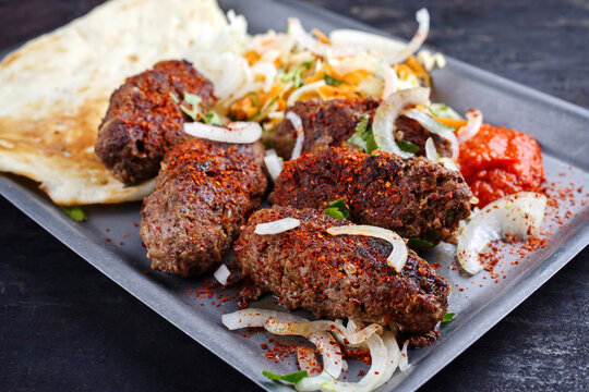 Traditional Croatian cevapi spicy meat ball rolls with cabbage carrot salad, pita bread and hot ajvar sauce served as close-up in a metal tray