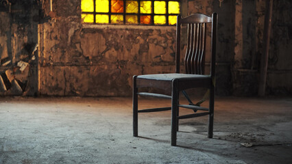 Fototapeta na wymiar wooden old chair stands in middle of abandoned building or factory with yellow stained glass window, mid afternoon, yellow light falls on seat. concept of loneliness and post-apocalypse.