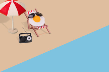 Creative funny composition made of sun umbrella, radio, fried egg with sunglasses sitting on deck...