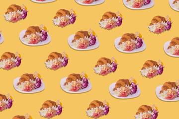 Creative pattern made of freshly baked croissant with flowers on pastel yellow background.
