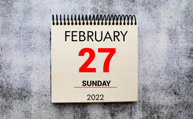 february 27. 27th day of month, calendar date. Stand for desktop calendar on beige wooden background.
