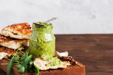 Green pesto sauce in a jar on a wooden board. - obrazy, fototapety, plakaty