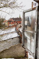 View through an open old wooden window to the historical buildings of Kuldiga Old Town in winter day, Latvia.