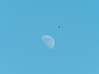 Flying red kite with blue sky and half moon background, focused on the kite.
