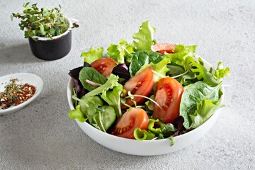 Fresh salad with fresh vegetables, ripe tomatoes, cucumber, lettuce and microgreen in a bowl on a gray background. Healthy raw food concept. Place for text, copy space.