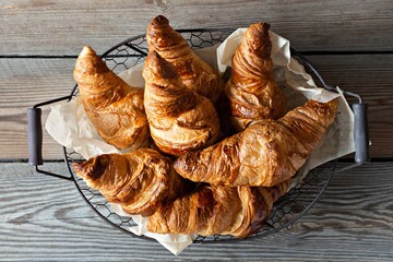 Fresh crispy french croissants in a basket on a wooden background. Traditional ruddy puff pastry...