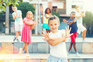 Fototapeta na wymiar Positive cute girl dancing modern choreography with group of tweenagers on city street on summer day..
