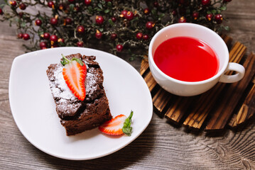 A portion of chocolate brownie and a cup of fruit tea to take time a have a break. On a wooden table top, a hot cup of tea. Wild artificial berries on a background.