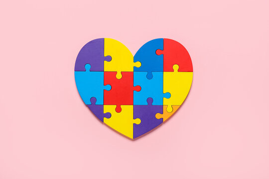 Colorful puzzle pieces in shape of heart on color background. Concept of autistic disorder