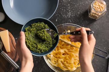 Woman adding pesto sauce in pasta on table in kitchen
