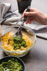 Woman adding pesto sauce in pasta on table in kitchen