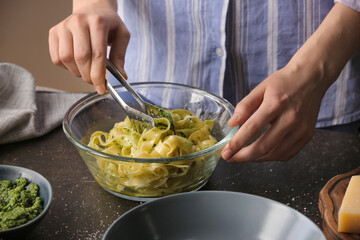 Woman making pesto pasta on table in kitchen
