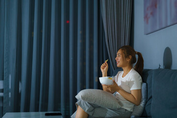 asian woman watching television suspense movie or news looking happy and funny and eating popcorn...