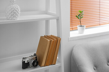Photo camera and books on shelf near light wall