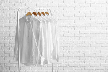 Rack with clean shirts in plastic bags on white brick background