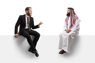 Businessman and a saudi arab man having a conversation seated on a blank panel