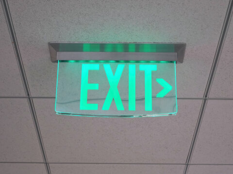Illuminated Overhead Green Exit Sign In Modern Office Building