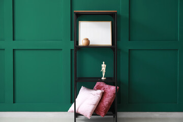 Shelf unit with decor, blank photo frame and pillows near color wall
