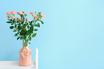 Vase with bouquet of beautiful fresh roses near blue wall