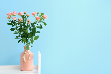 Vase with bouquet of beautiful fresh roses near blue wall