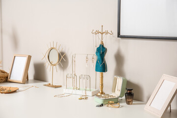 Different stands with stylish jewelry and photo frames on table near light wall