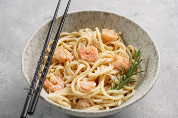 Deep grey japanese style bowl with pasta spaghetti with heavy cream and roasted shrimps with garlic sauce and parmesan cheese, black chopsticks on grey concrete surface