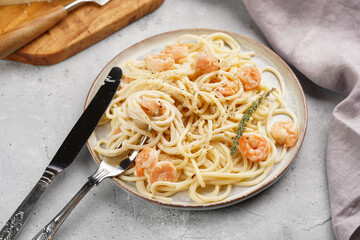 Flat plate with pasta spaghetti with heavy cream and roasted shrimps with garlic sauce and parmesan cheese on grey concrete surface