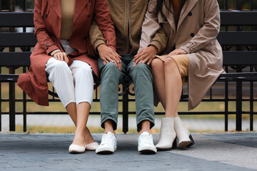 Man and two beautiful women sitting on bench in park. Polyamory concept