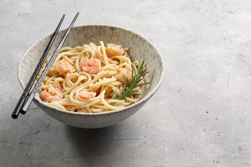 Deep grey japanese style bowl with pasta spaghetti with heavy cream and roasted shrimps with garlic sauce and parmesan cheese, black chopsticks on grey concrete surface