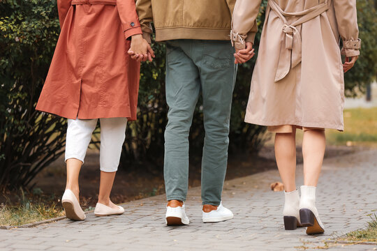 Man with two beautiful women walking in park. Polyamory concept
