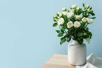 Vase with bouquet of beautiful roses on table near blue wall