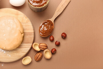 Wooden board of fresh dough for preparing walnut shaped cookies with boiled condensed milk and ingredients on brown background, closeup