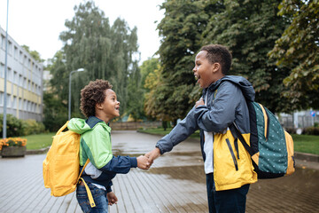 Two African American boys next to the school. Schoolboys with backpacks. Back to the school concept. Kids standing outside and happy to meet each others. Happy black children. First day of school