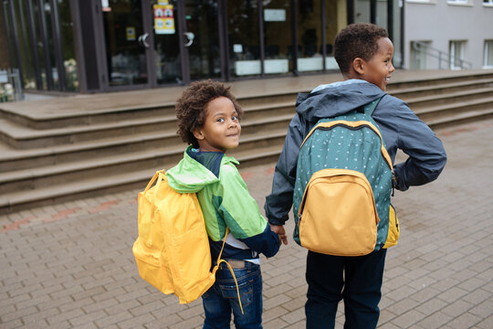 Two African American boys next to the school. Schoolboys with backpacks. Back to the school concept. Kids standing outside and happy to meet each others. Happy black children. First day of school