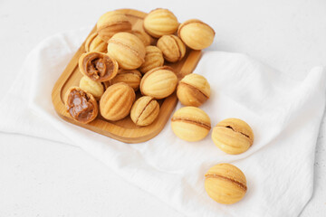 Wooden board of tasty walnut shaped cookies with boiled condensed milk on light background